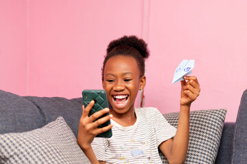 young African little girl holding up a paper airplane and mobile phone in hand