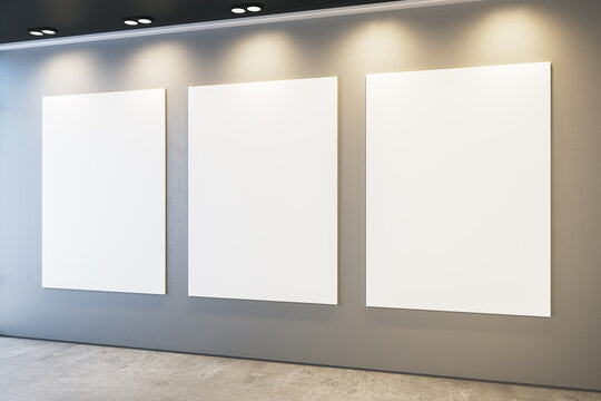 Modern museum or exhibition hall interior with illuminated empty white mock up frames on concrete wall. 3D Rendering.