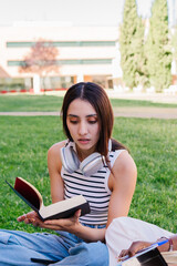 Obraz premium Concentrated student reading a book sitting on the grass of the university campus