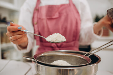 Happy young cook girl wearing apron, using mobile phone in home kitchen while baking pie, pizza, pastry, taking photo of raw bakery food for blog, chatting, making call