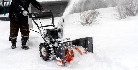 snowblower removes snow, a man cleans the yard outside
