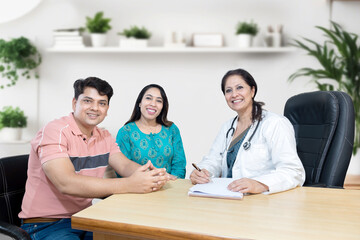 Portrait of Indian female gynecologist doctor consulting young married couple patients in fertility clinic about IVF or IUI. Planning pregnancy concept.
