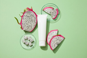 White cosmetic tube featured on green background with dragon fruit slices surrounded. Natural...