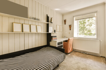 a bedroom with a bed, desk and books on the shelf above the bed is a window that looks out onto the street
