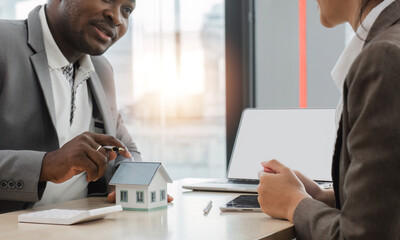 Agents and clients discuss contracts to buy, insure, or borrow real estate or assets. along with viewing a sample house model.