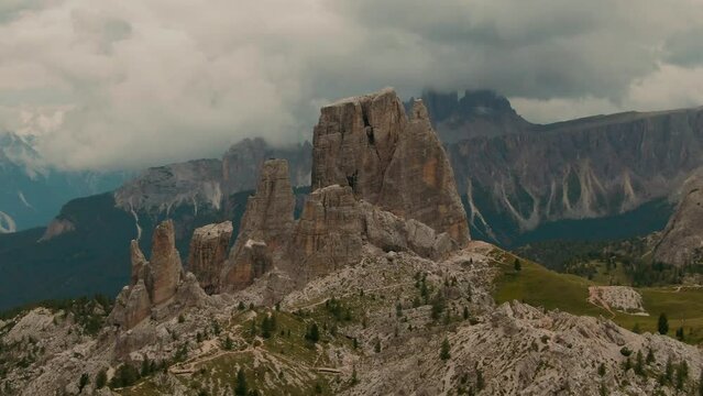 Parallax drone shot massive rock formations with distant tall mountains in the background, green forest at the bottom, cloudy day, cinematic color grade