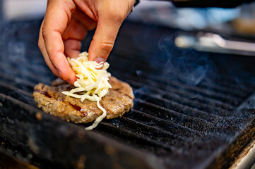 man hand cooking cheeseburger on grill