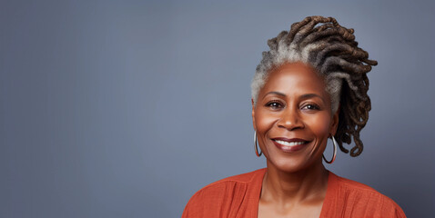 Studio headshot portrait of smiling mature black woman with dreadlocks, gray background