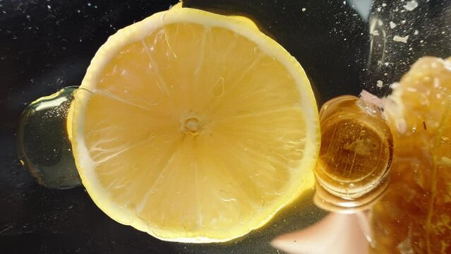 A lemon slice in a clear glass dish, I scoop honey with a wooden spoon, close-up from below.