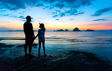 Silhouette Asian father and teenage daughter holding hands talking, standing together on sunset beach. Daddy and child girl hand in hand. Fathers day concept, Tub Kaek beach,Krabi,Thailand. Copy space