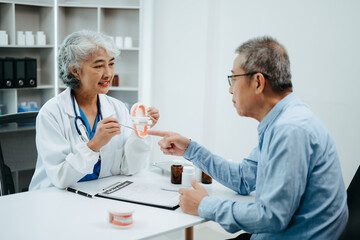 Fototapeta premium Concentrated dentist sitting at table with jaw samples tooth model and working with tablet and laptop in dental office professional dental clinic.