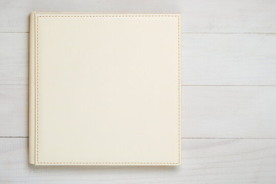Family photo album on the wood table. Photo book from white color eco leather, top view.