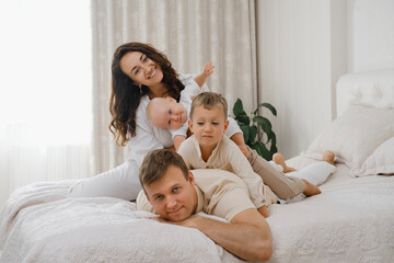 Obraz na płótnie Canvas Family with two kids on the bed having fun. Mather, father baby and toddler sons are happy in the morning in bedroom. Children playing on fathers back. Real life and happiness 