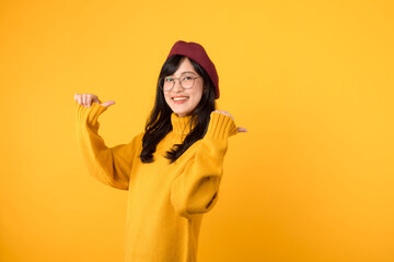 young Asian woman in her 30s, wearing a yellow shirt and red beret. happy face and pointing finger to free copy space against vibrant yellow backdrop. Unlock savings and shop now!