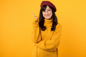 Cheerful young woman 30s wearing yellow sweater use finger pointing to product or empty copy space while standing over isolated on yellow background.