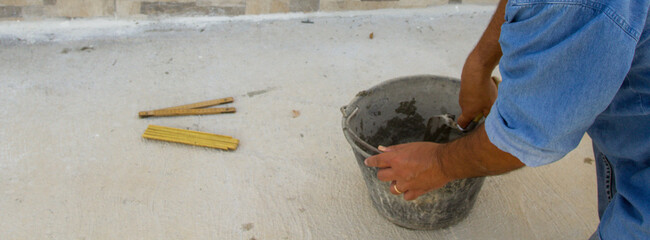 Image of a bricklayer's hands mixing cement and glue in a bucket. Manual masonry and tiling work. Horizontal banner