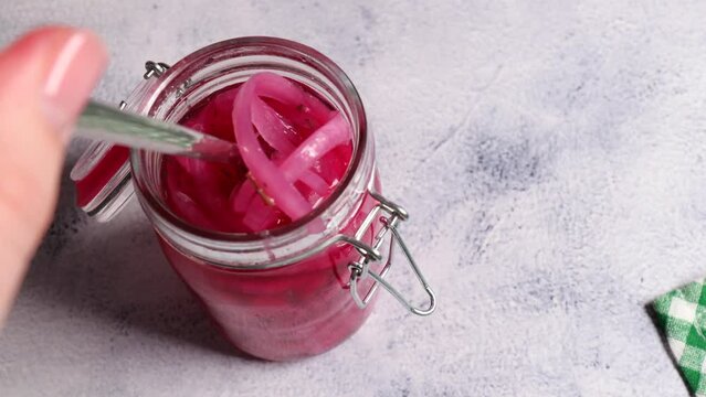 The girl takes the onion out of the jar with a fork. Pickled purple onion rings in an open glass jar in the kitchen. selective focus
