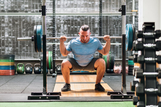 Strong sportsman doing squat exercises in gym light with barbell