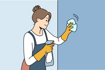 Housewife woman cleaning apartment, wiping wall or glass using antibacterial spray, dressed in apron and gloves. Happy girl works as maid in motel and cleaning preparing room for arrival of guests