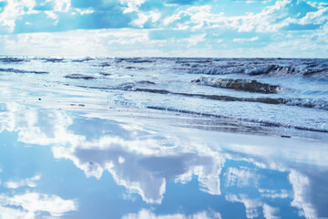 Fabulous view of mirror-smooth water of seashore coastline near waves reflecting blue sky, white clouds on sunny day.