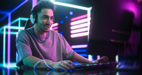 Young Excited Gamer Playing Online Video Game on a Computer. Portrait of a Handsome Man in Headphones Battling in PvP Tournament with Other Players, Talking with Team on Microphone