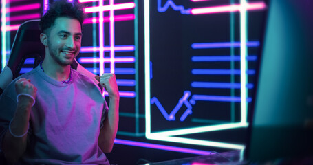 Excited Handsome Man Playing Video Games with Friends on a Computer, Surrounded by Cyberpunk Style Background. Young Gamer Winning the Round and Celebrating