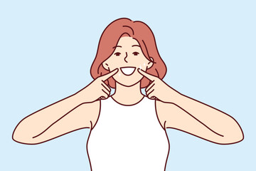 Woman smile and shows off white teeth and points fingers at mouth to invite people to dental clinic. Positive girl is trained to make big smile to appear friendly for successful sales