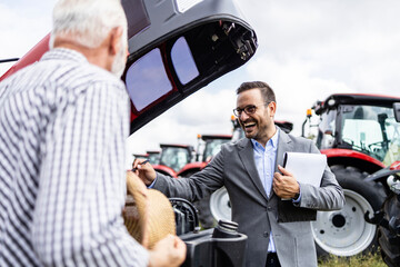 Tractor dealer showing specification of modern agricultural machines to the farmer at dealership.