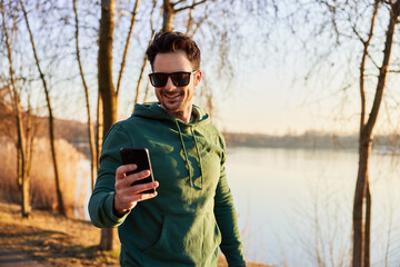 Happy man in park using phone during outdoors running exercises