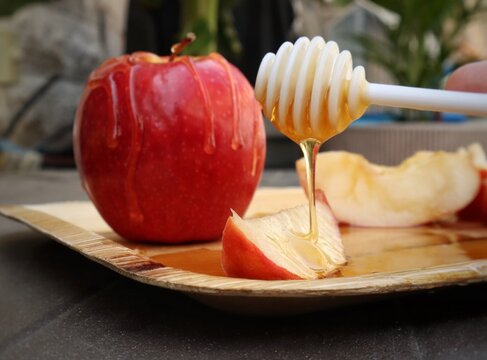 Shana Tova. Apple. Honey. Apple dipped in honey. Cut up apple and dripping honey dipper. red apple dip in honey. Jewish new year concept. Honey. Rosh Hashana Concept.  Dip the apple in the honey.
