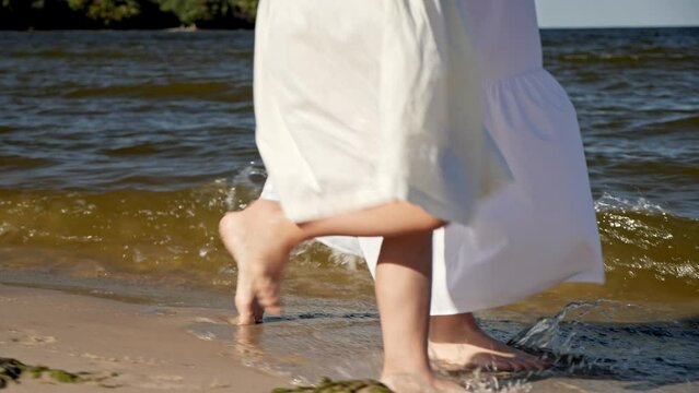Mom and daughter in dresses walking along the beach, close-up of legs