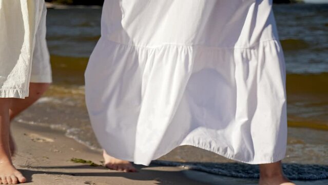 Mom and daughter in dresses walking along the beach, close-up of legs
