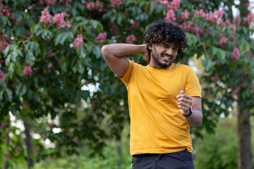 Indian young man walks in the park, does sports. Suffering from itching and mosquito bites, grimacing from discomfort