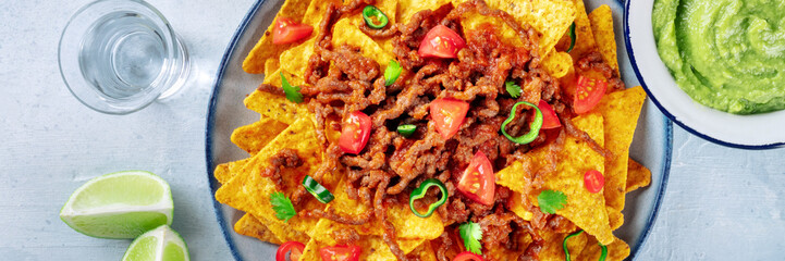 Nachos panorama, Mexican food, tortilla chips with beef and fresh vegetables, overhead flat lay shot with tequila, limes, and guacamole