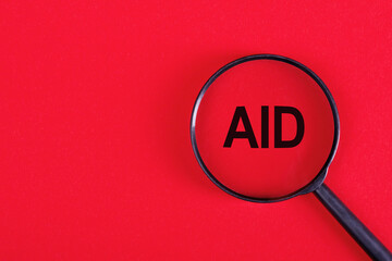 The word AID under magnifier on red background