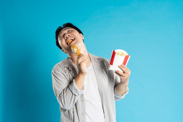Portrait of asian man eating fast food on blue background