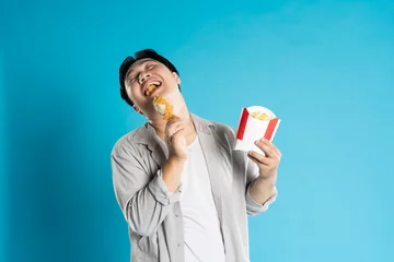 Fotobehang Portrait of asian man eating fast food on blue background © 1112000