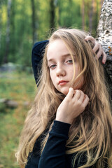 Naklejka premium Close-up portrait of a romantic 13-15 year old girl in the woods. A girl with long blond hair looks at the camera