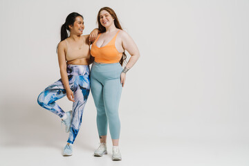 Two smiling women in sportswear posing together isolated over white wall