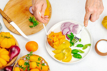 A woman is preparing a tomato salad. Ripe vegetables, herbs, aromatic spices, olive oil