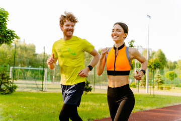 Athletic man and woman smiling while running together in park