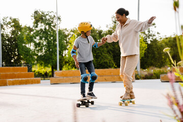 Smiling woman and her son holding hands while riding skateboards at skatepark