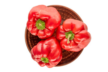Three red sweet peppers on a clay plate on a white background, macro, top view.