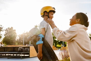 Foto auf Acrylglas Smiling mother putting safety helmet on her son at skatepark © Drobot Dean