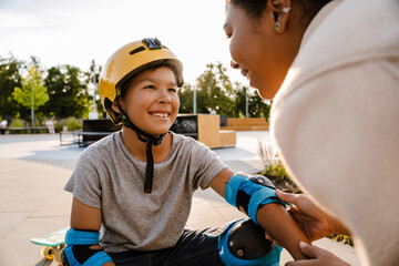 Naklejka premium Smiling mother putting safety gear on her son at skatepark