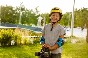 Poster Smiling boy wearing safety helmet holding skateboard while standing in park © Drobot Dean