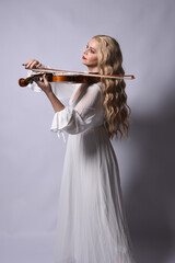 Close up portrait of beautiful blonde model wearing elegant  white halloween gown, a historical fantasy character.  Holding a violin musical instrument, isolated on studio background.