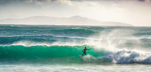 A man surfing on a wave at Crescent Head in NSW on a summer's day. The shot is backlit and the wave...