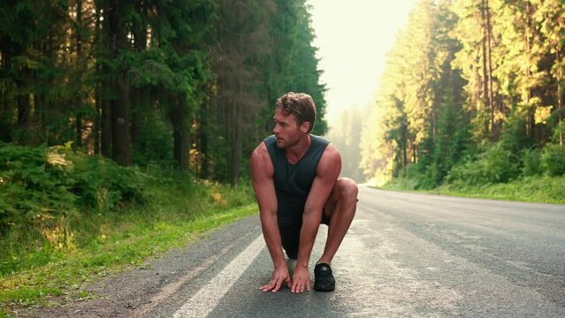 Curly haired meditative blond athlete doing stretching exercise on the road before run in the forest