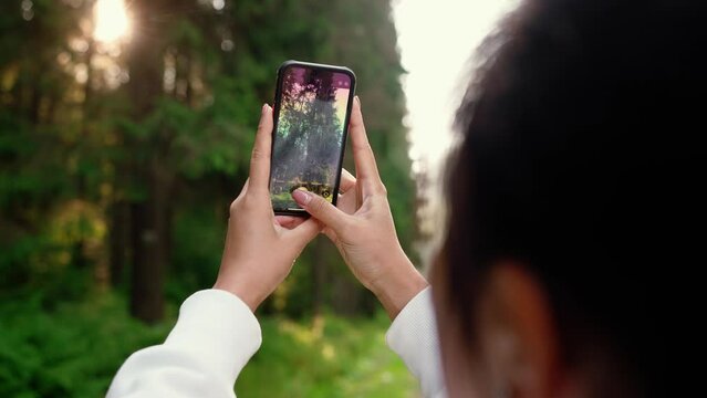 Back view of woman takes picture of forest with her phone after run outdoors
